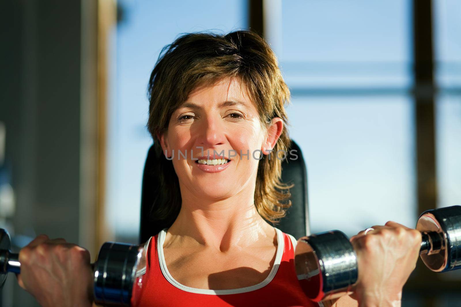 Mature woman lifting dumbbells exercising in a gym; focus on her face