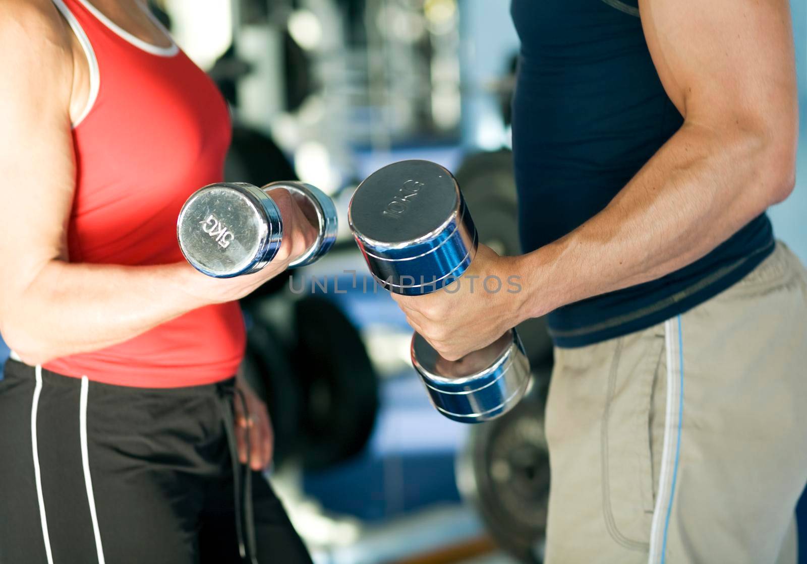 man and woman (only arms and body) lifting dumbbells (shallow depth of field, focus only on hands)