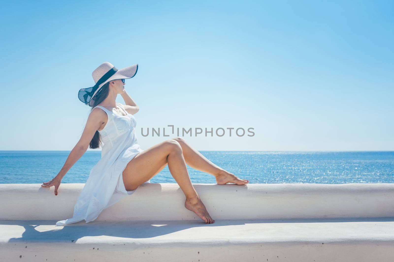 Woman sitting in the sun on a greek beach looking at the sea