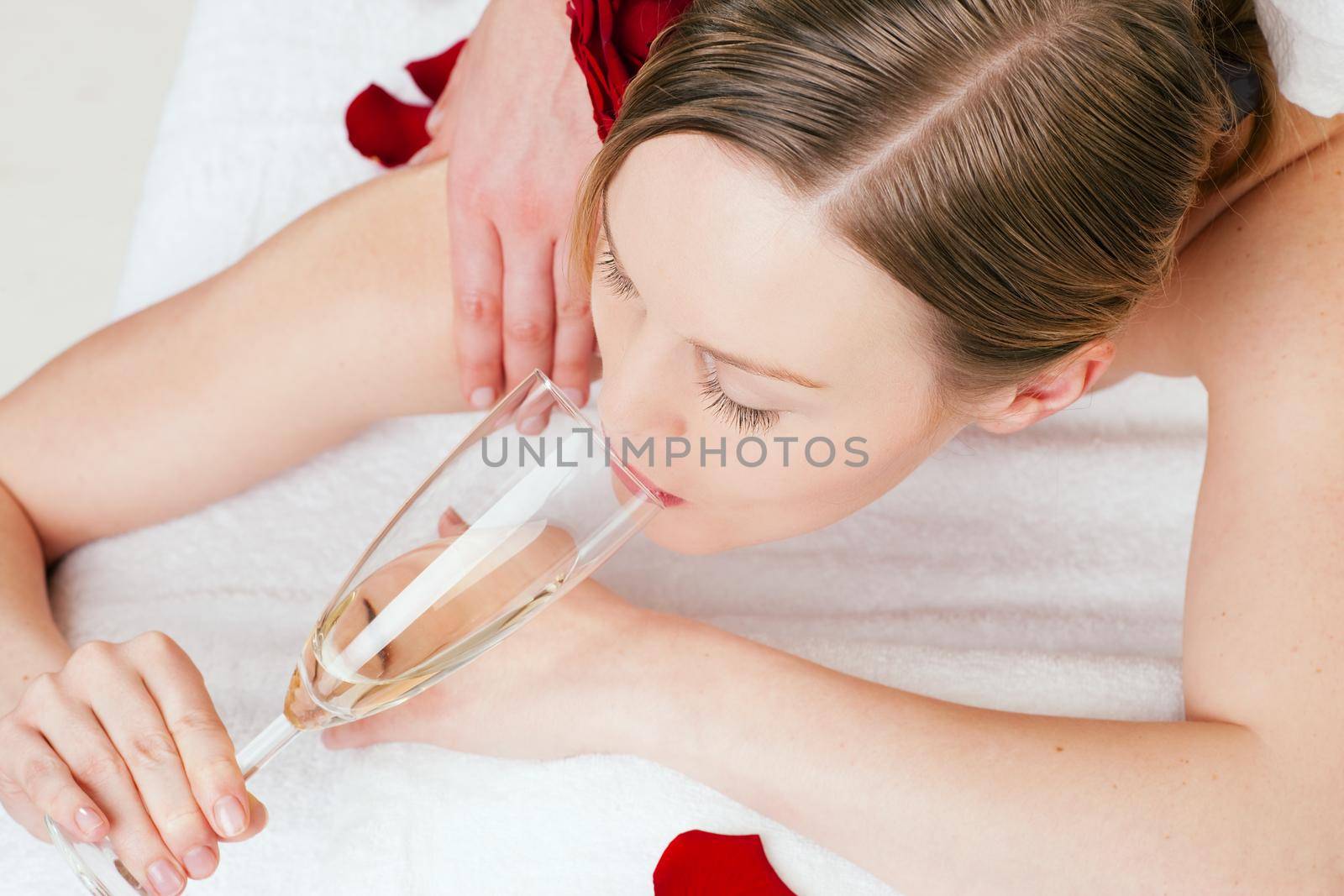 Woman enjoying a back massage in a spa setting drinking a glass of champagne