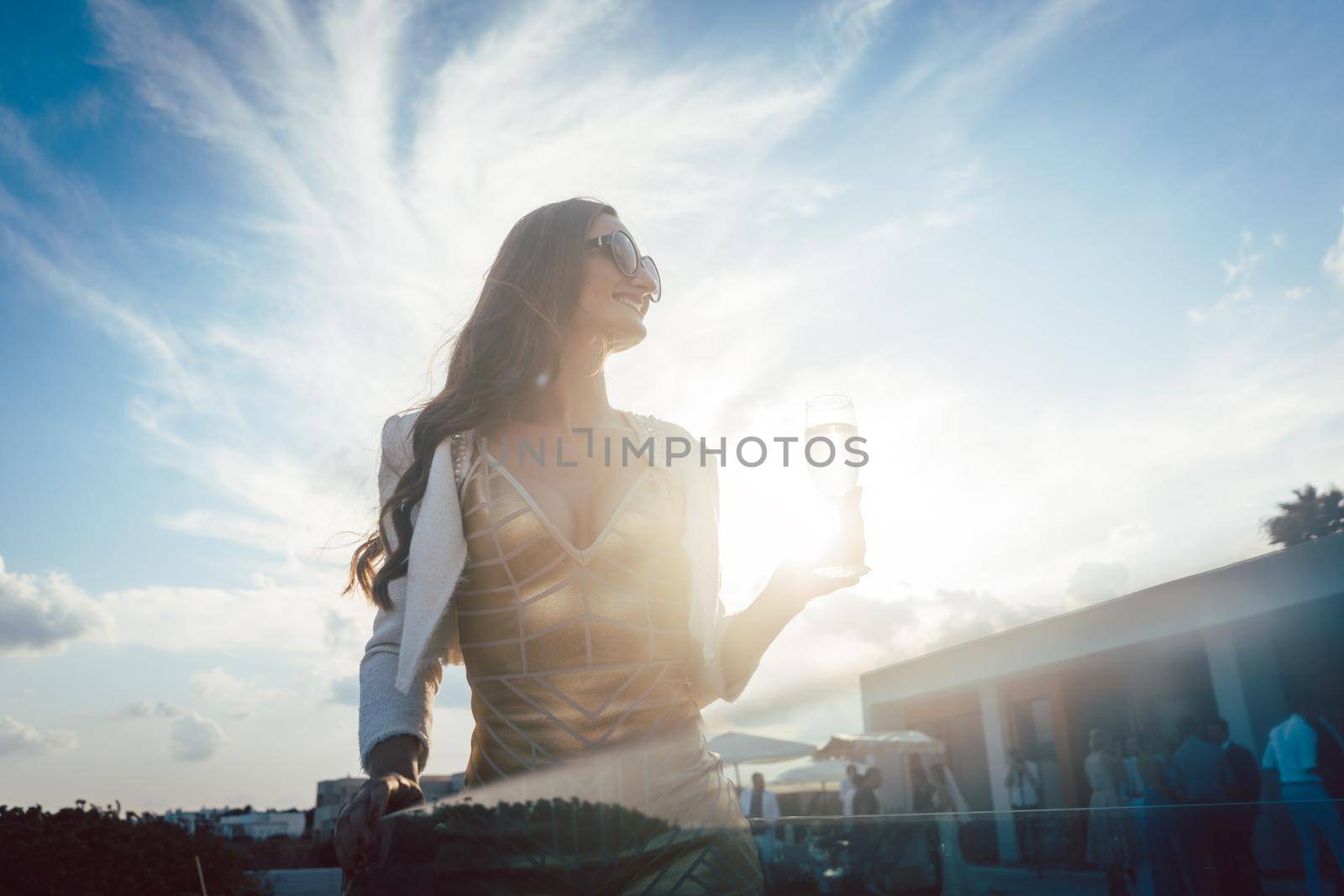 Woman having champagne at summer party with villa in the background