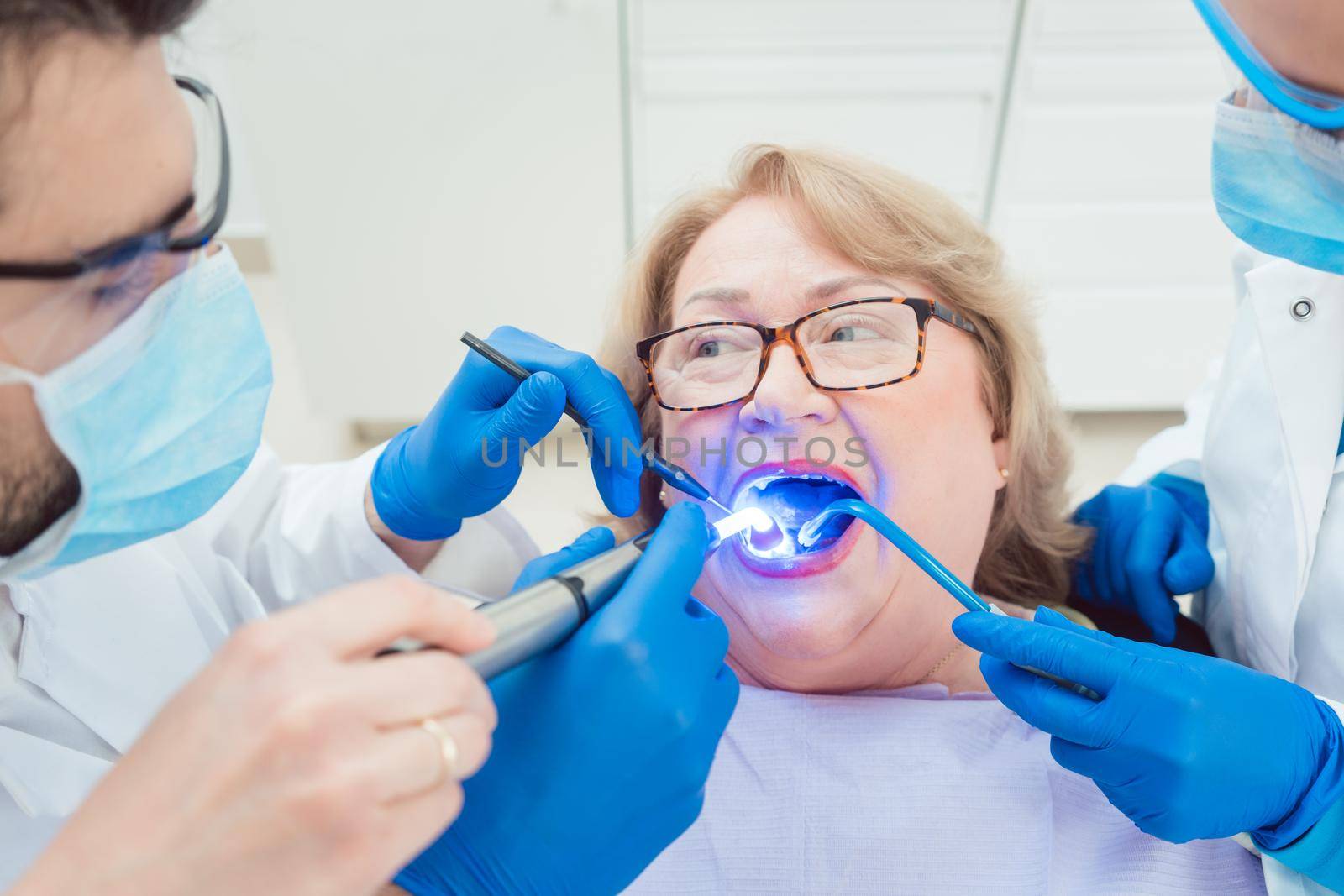Dentists hardening toot crown with UV light treating senior patient