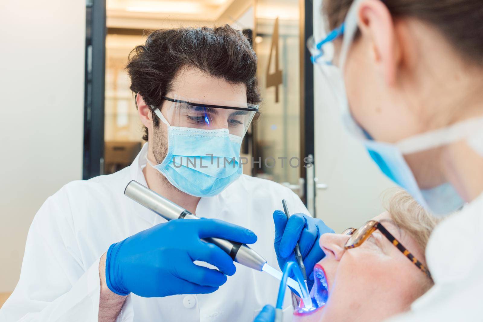 Dentists hardening toot crown with UV light treating senior patient