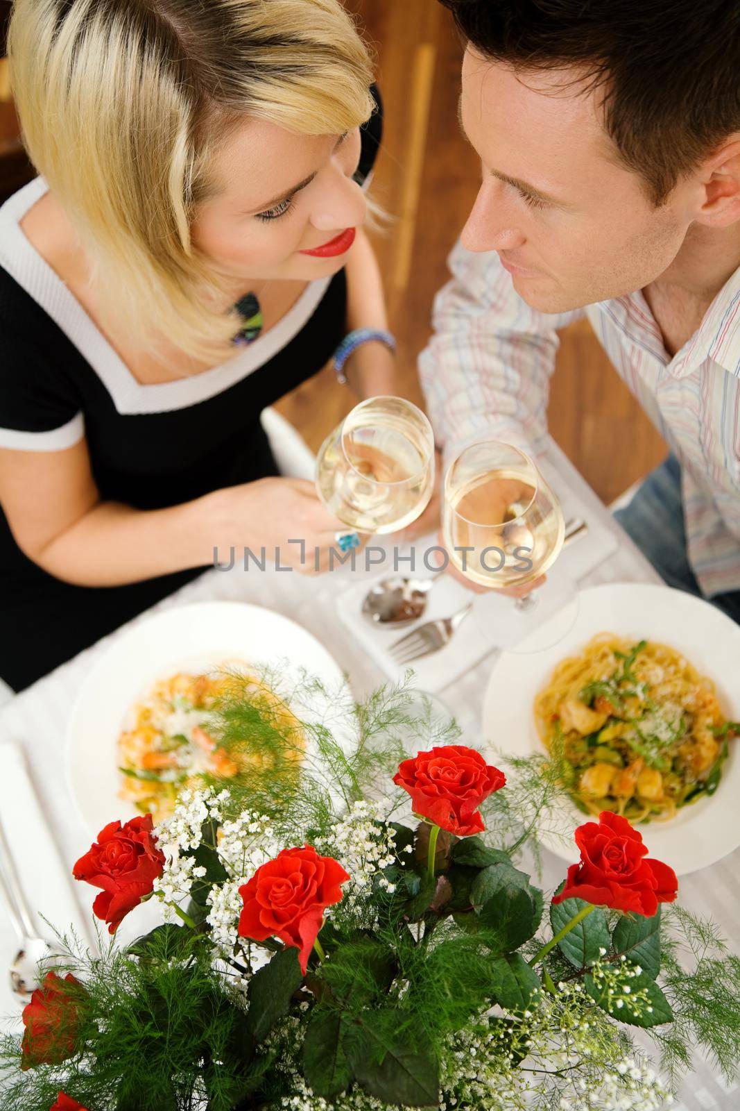 Young couple romantic dinner: letting the white wine glasses clink; focus on the eyes of the people