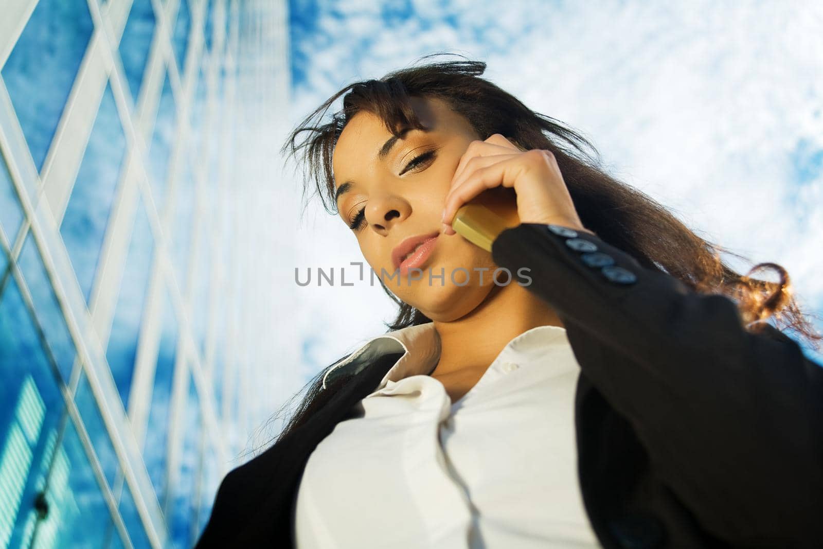 A brunette woman in business clothes using her mobile in front of a modern business building