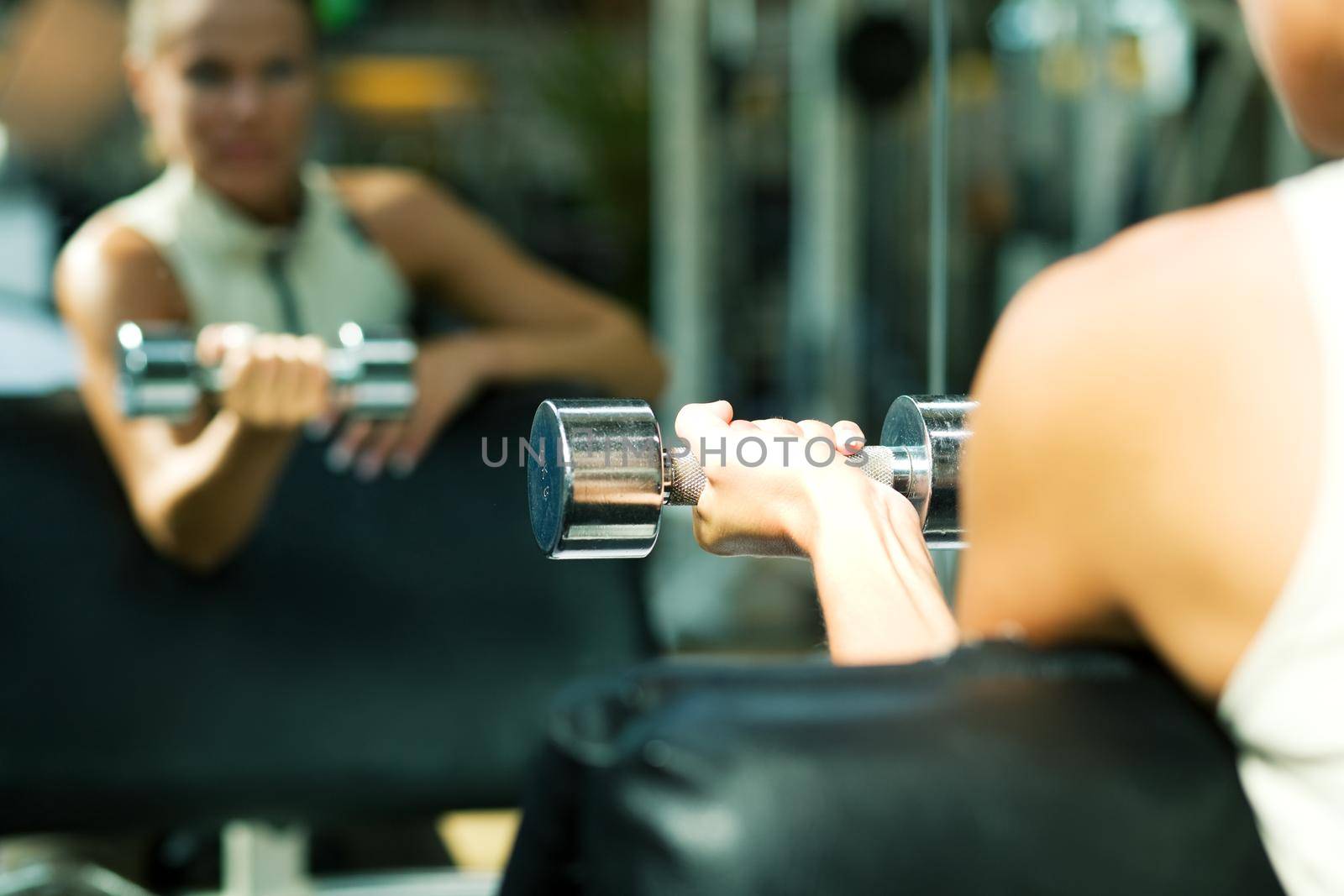 Woman lifting dumbbells in a gym, seeing herself in a mirror (focus only on the dumbbell)