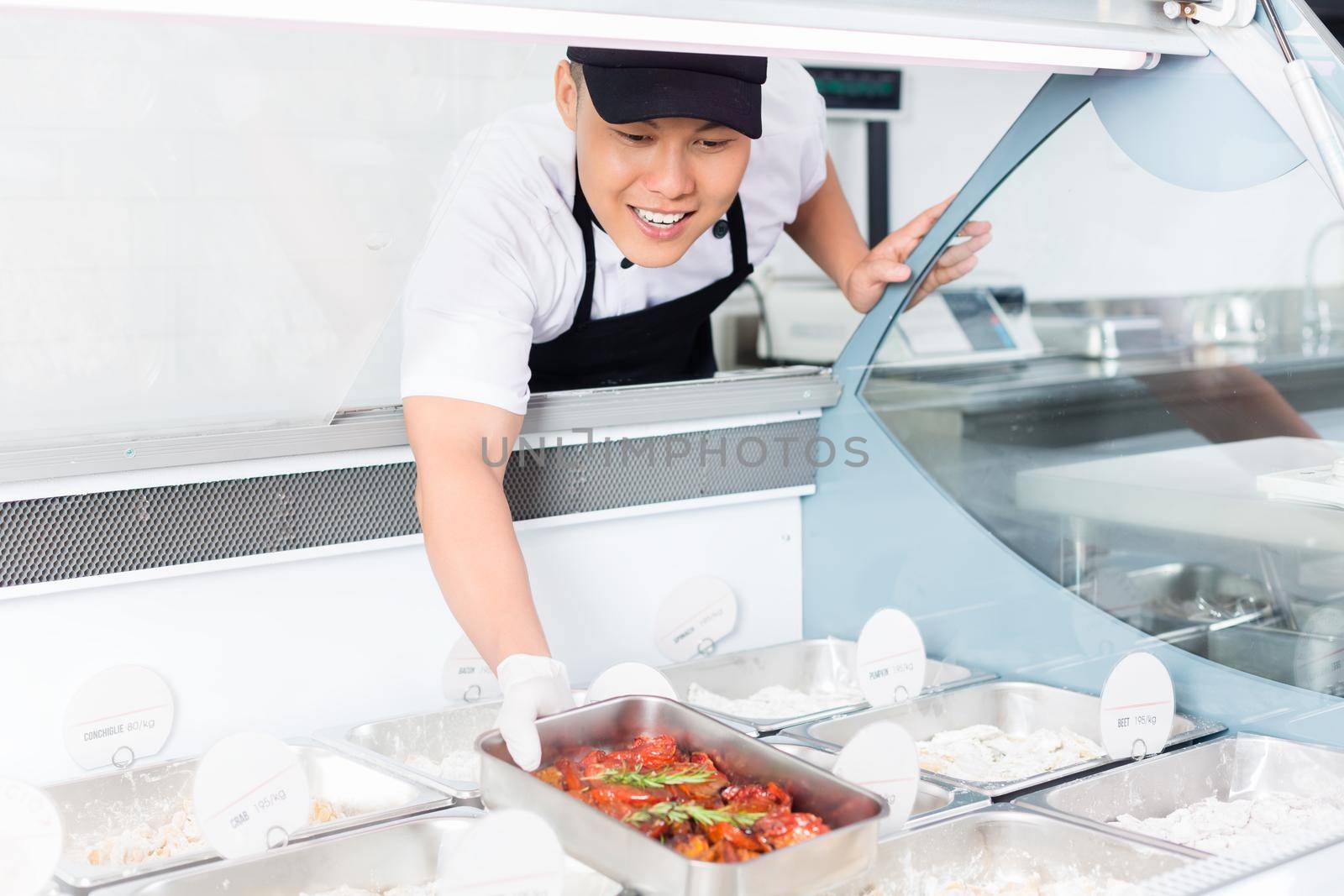 Chef replenishing a tray of food in a display in a delicatessen or restaurant reaching down into a large glass counter