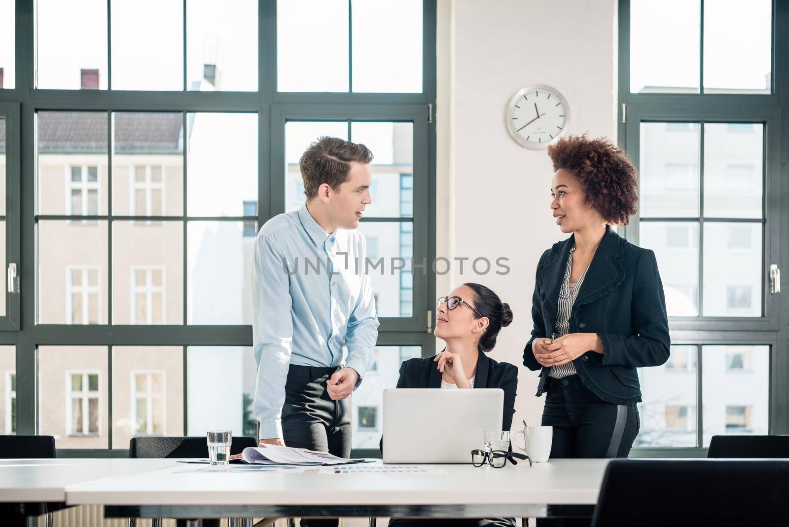 Three young colleagues talking during break in the meeting room of a modern business building