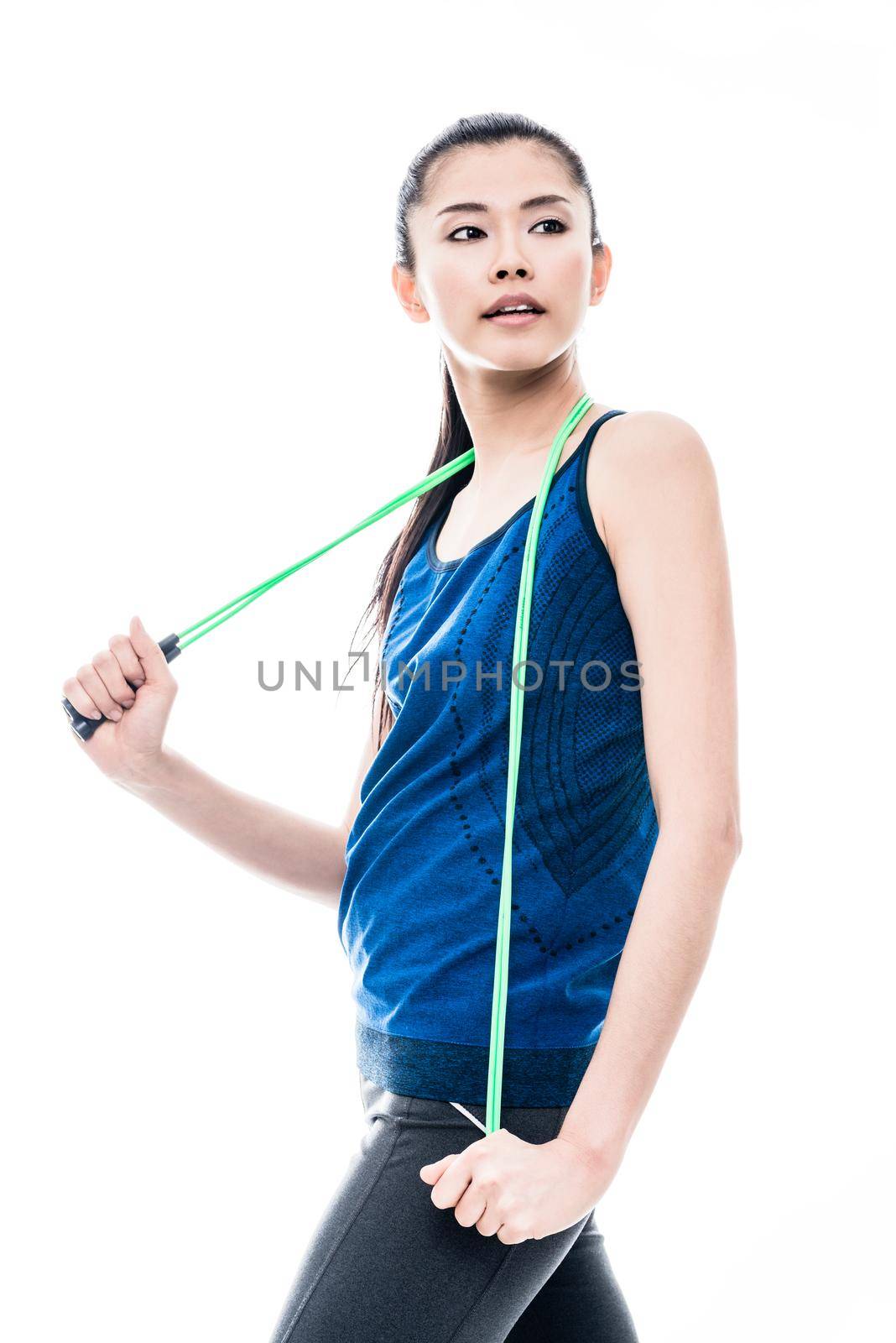 Fit young Asian woman with a skipping rope slung around her neck standing looking back over her shoulder with a pensive expression, three-quarter isolated on white