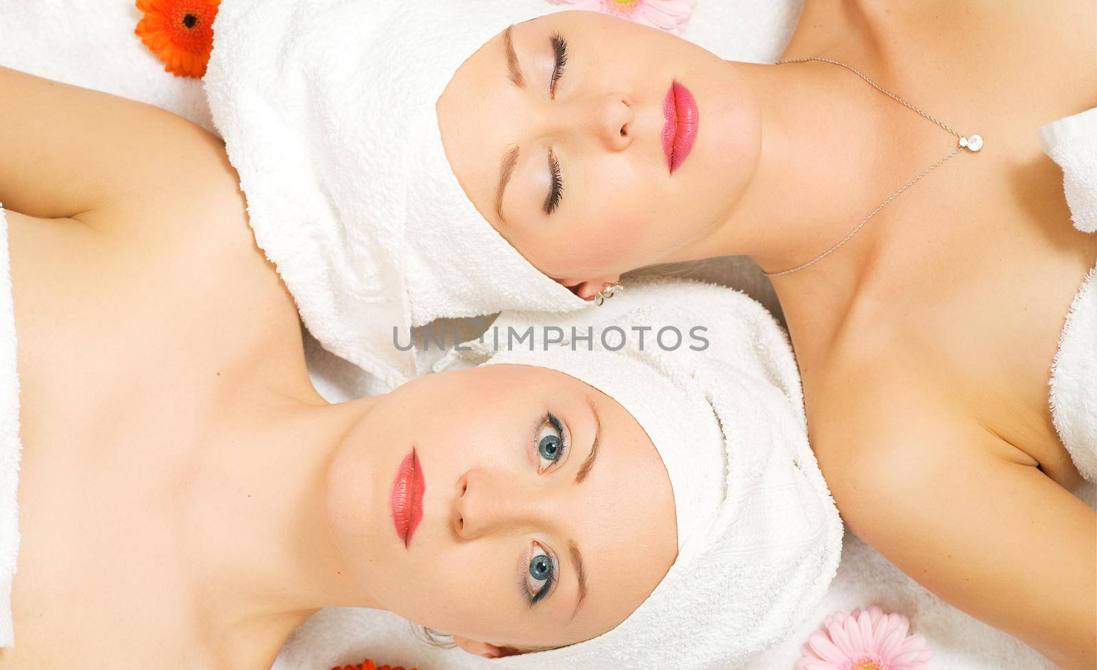 Two girls relaxing in a wellness set-up seen from above, horizontally aligned, with some flowers, closed eyes