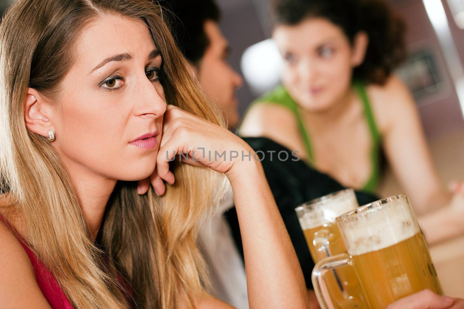 Group of people in a bar or restaurant drinking beer, woman in front being sad since her boyfriend is flirting with another girl dumping her