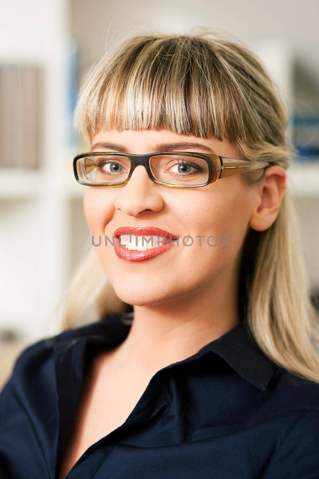Portrait of a young woman with glasses sitting in front of a book shelf