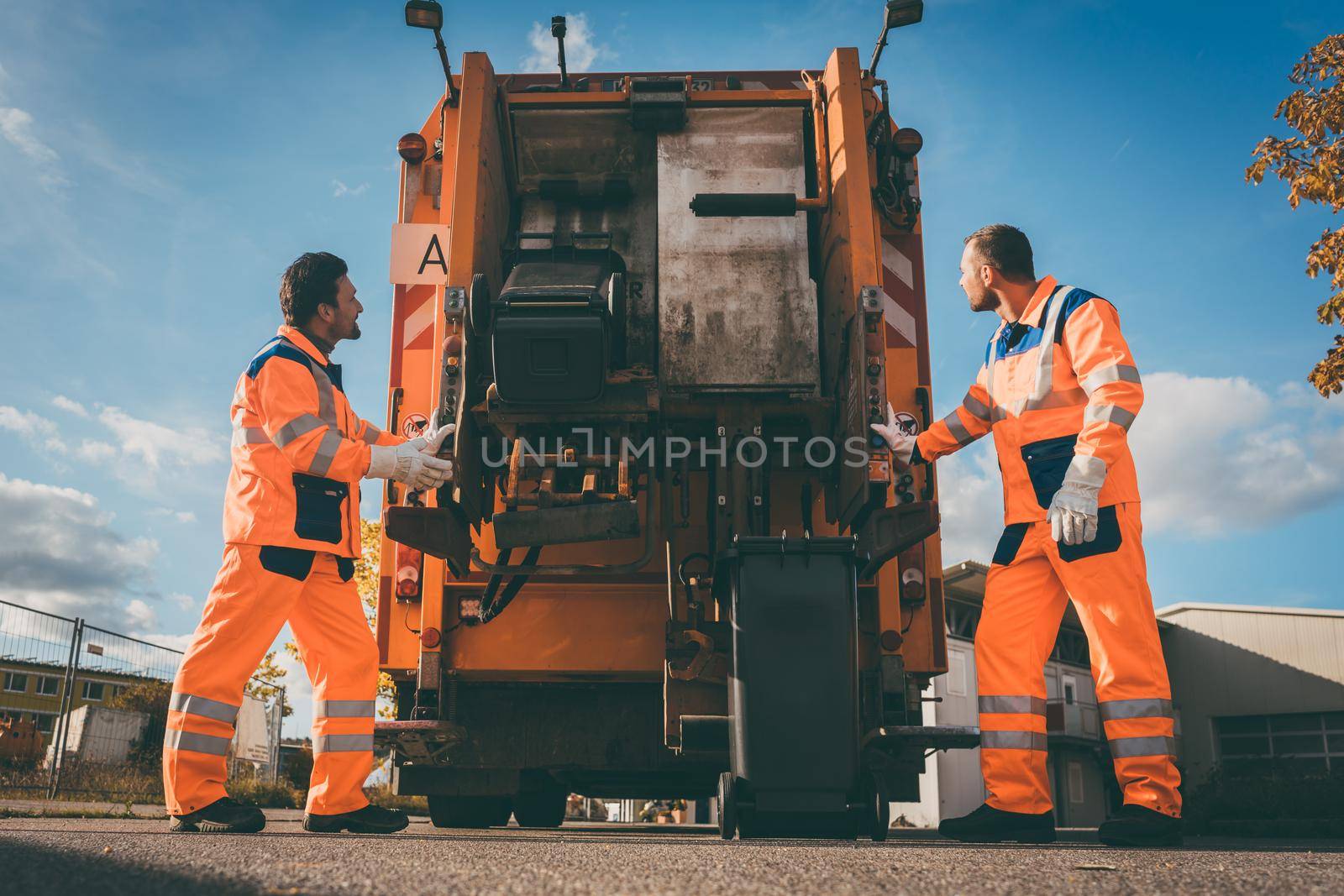 Two refuse collection workers loading garbage into waste truck by Kzenon