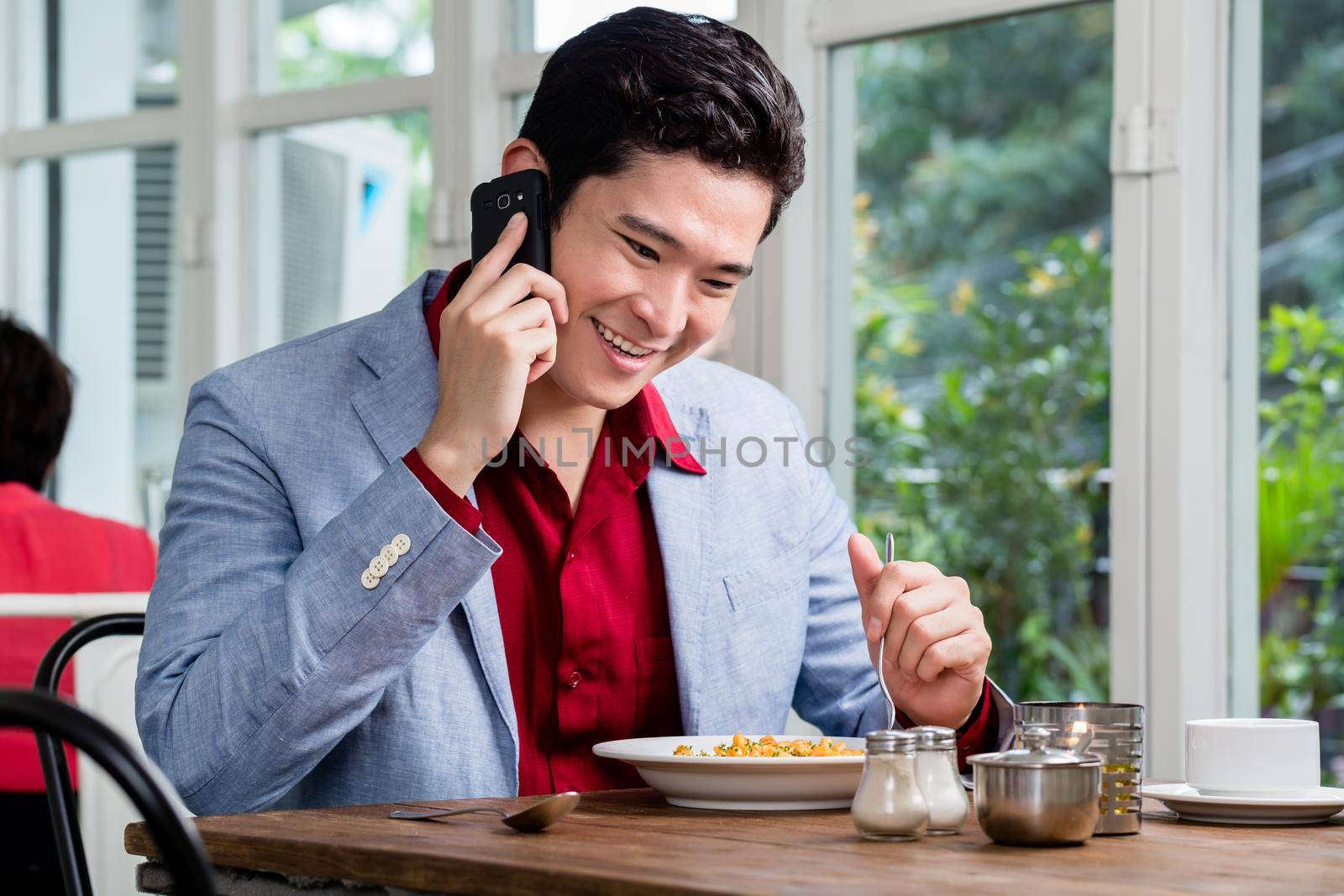 Handsome stylish formal young businessman talking on a mobile phone as he sits at a restaurant table enjoying lunch