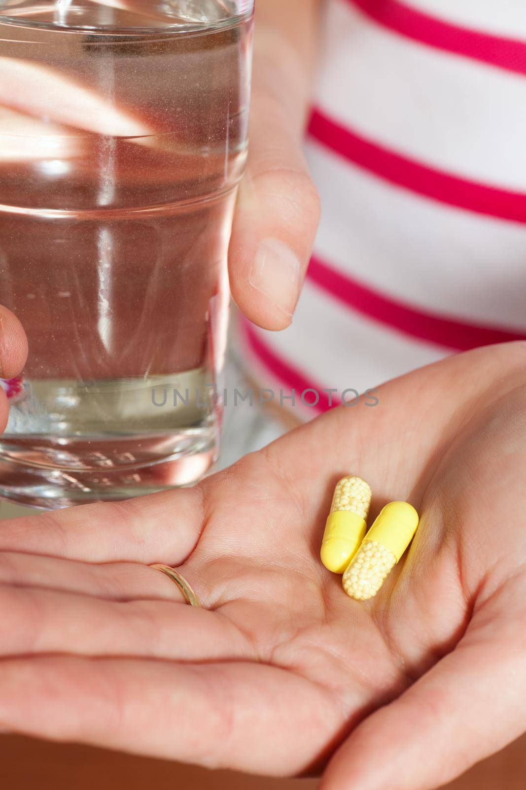 Woman holding pharmaceutical pills and a glass of water in her hand