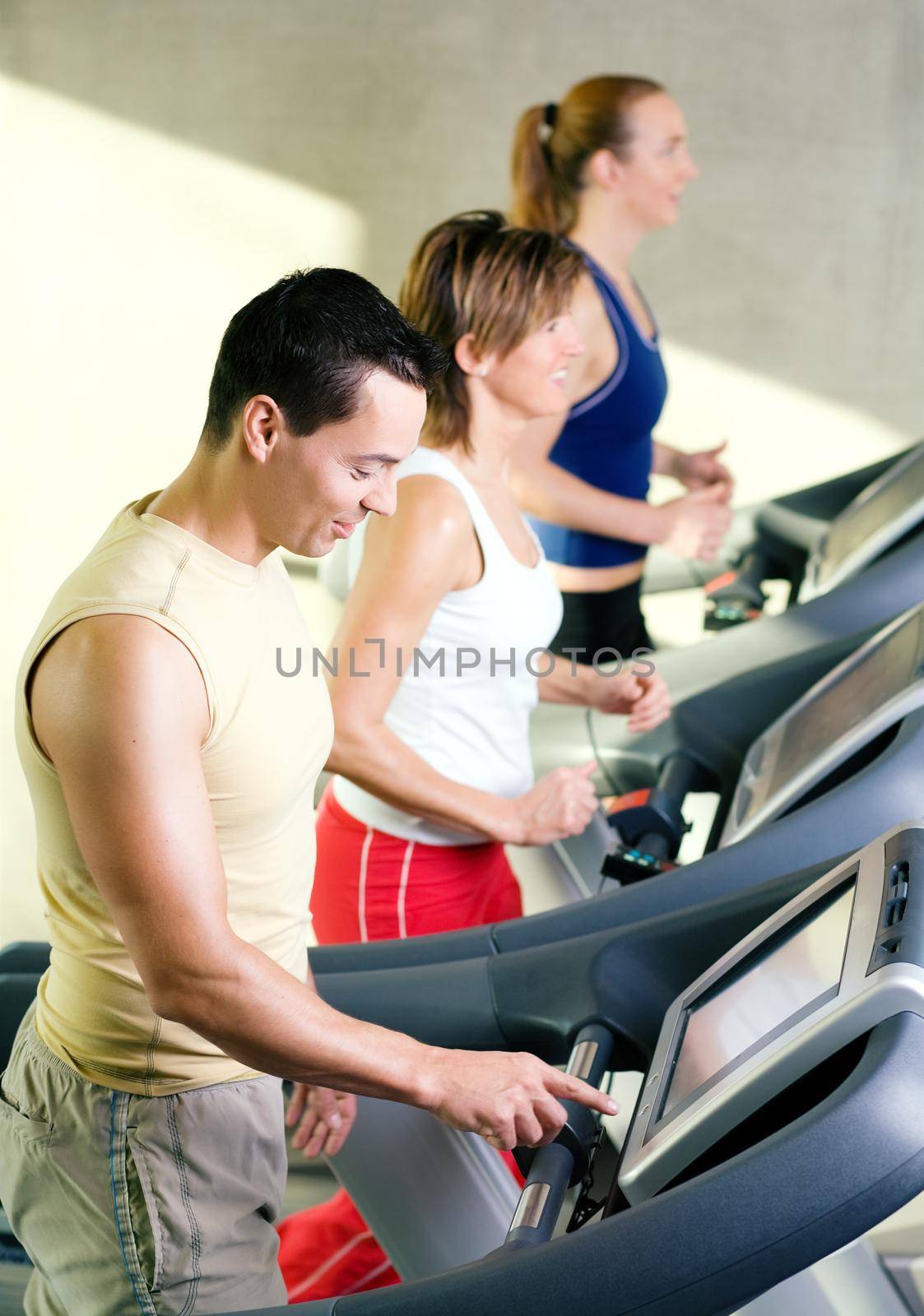 Three people on the treadmill in a gym, one choosing the program on the machine