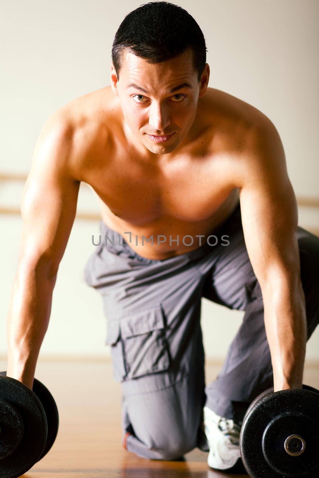 Strong man with dumbbells kneeling on the floor in a gym