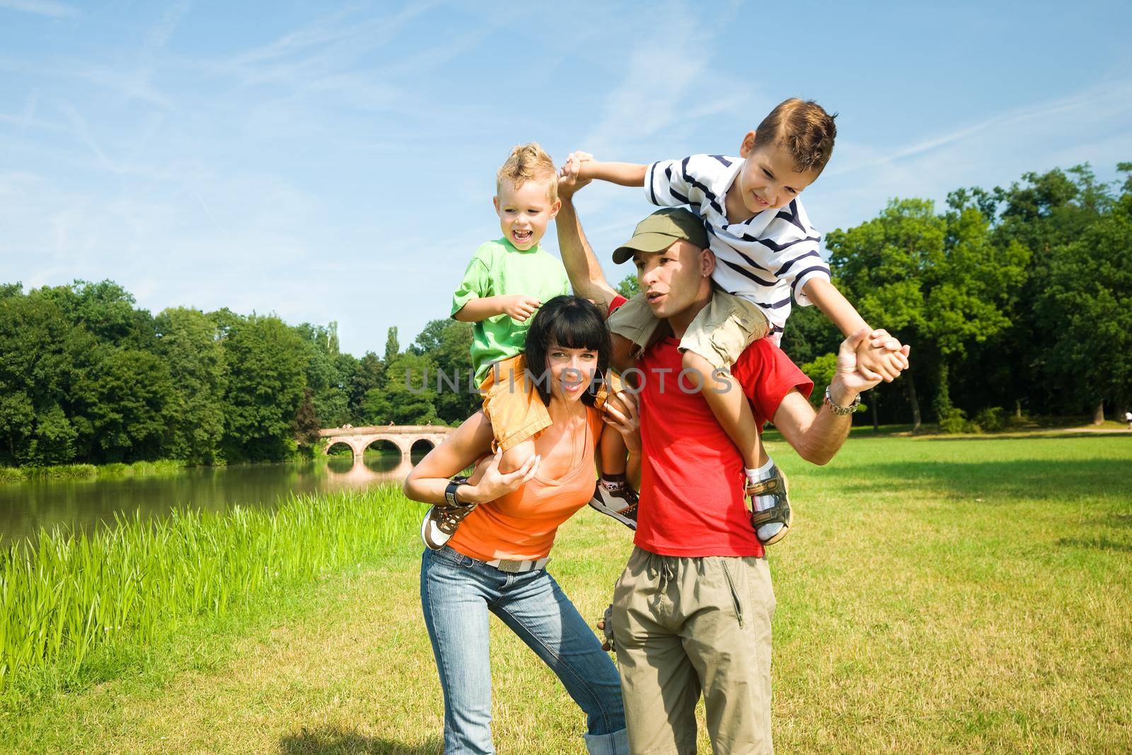 Family with two kids in a Park at a lake, carrying their children piggyback and having fun