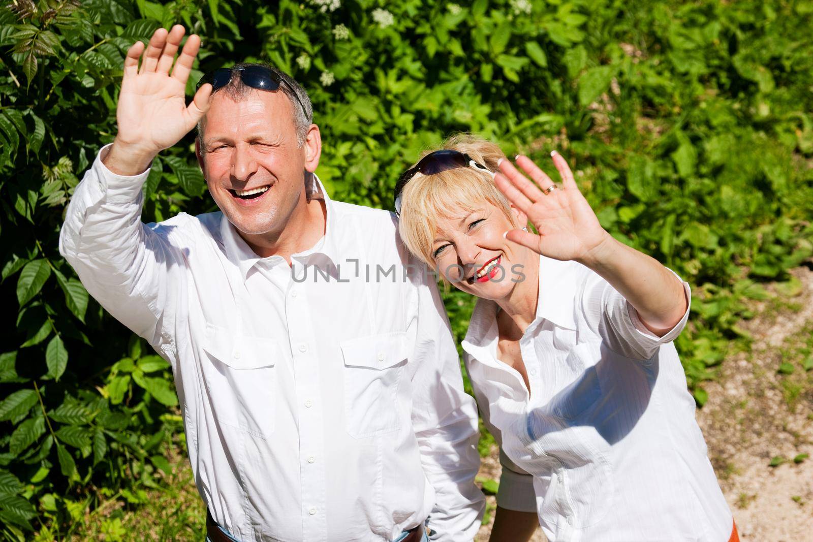 Happy senior couple outdoors waving hands by Kzenon