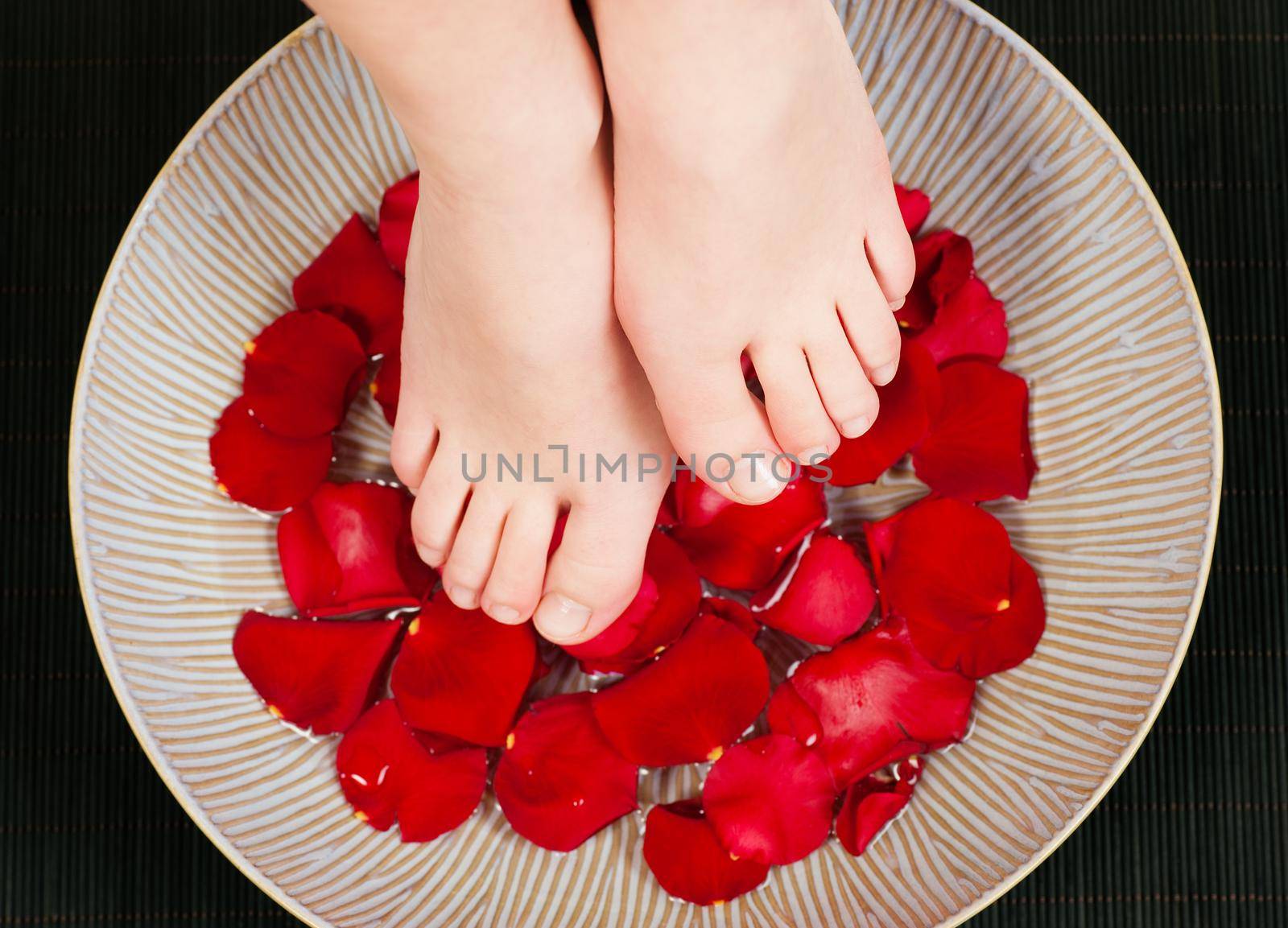 Feet in / above a bowl with water and rose petals - metaphor for wellness and pedicure