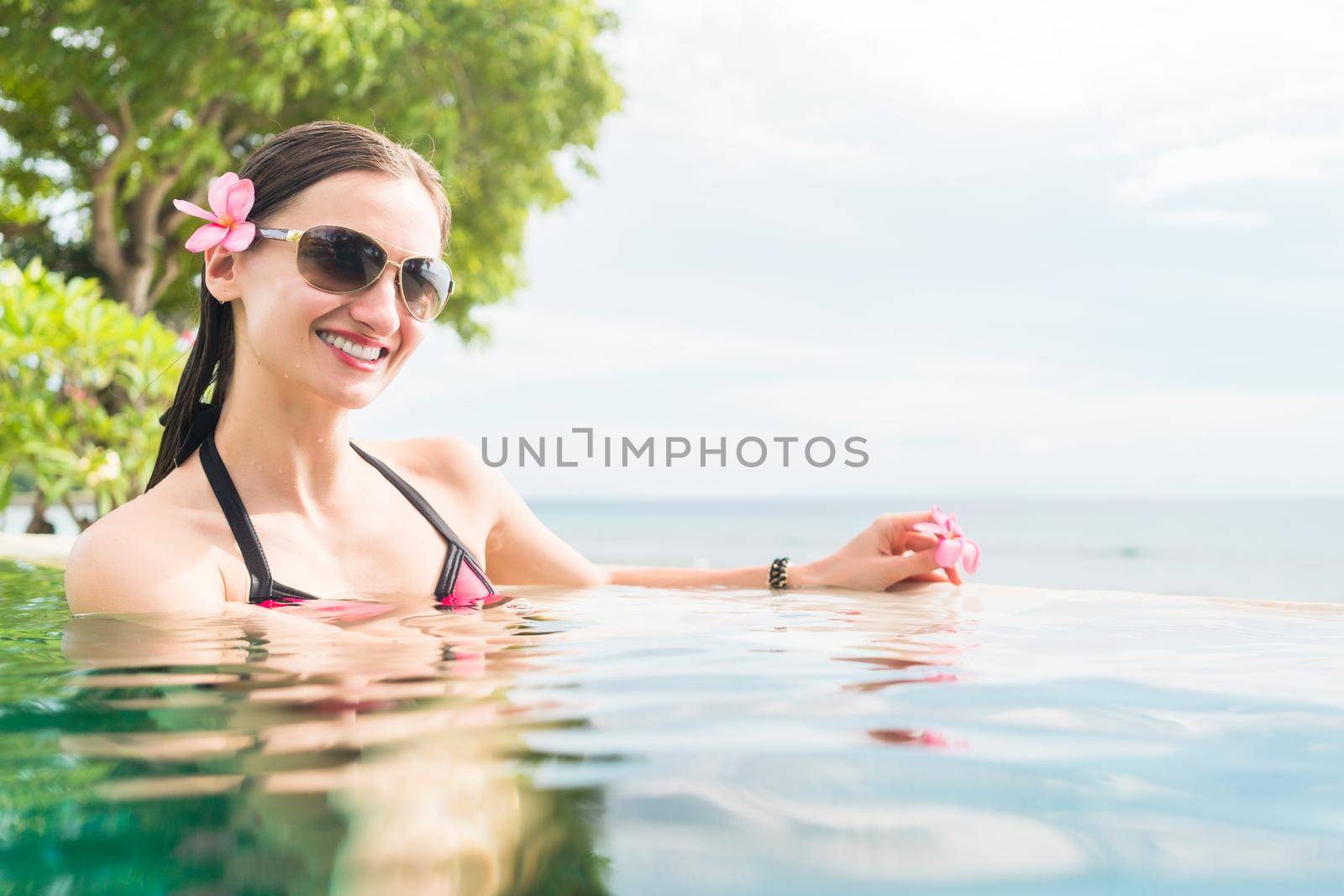 Woman in summer vacation relaxing swimming in pool with the ocean in the background