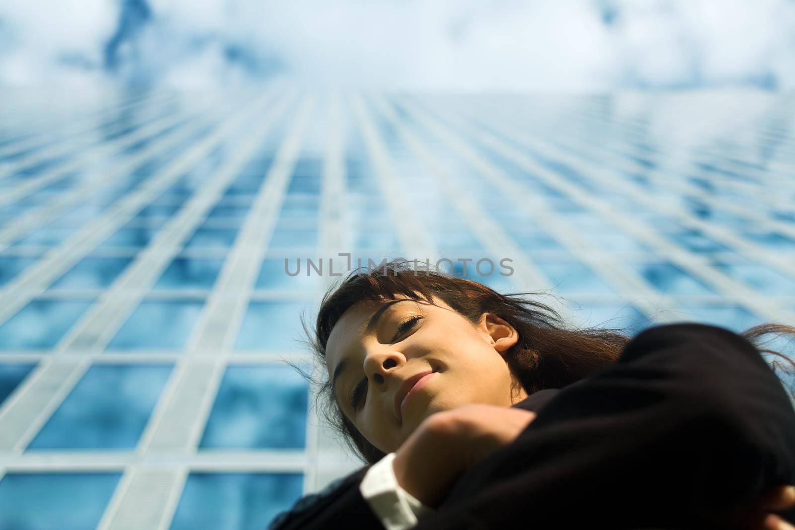 A young woman in a suit looking down to the viewer in front of a modern office building