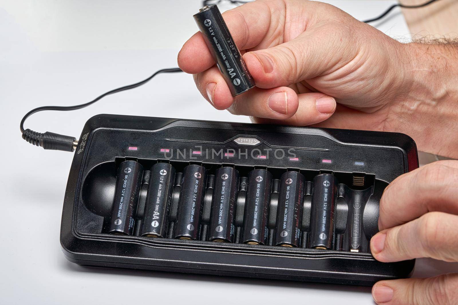 Hands insert AA batteries into black long charger. Close up