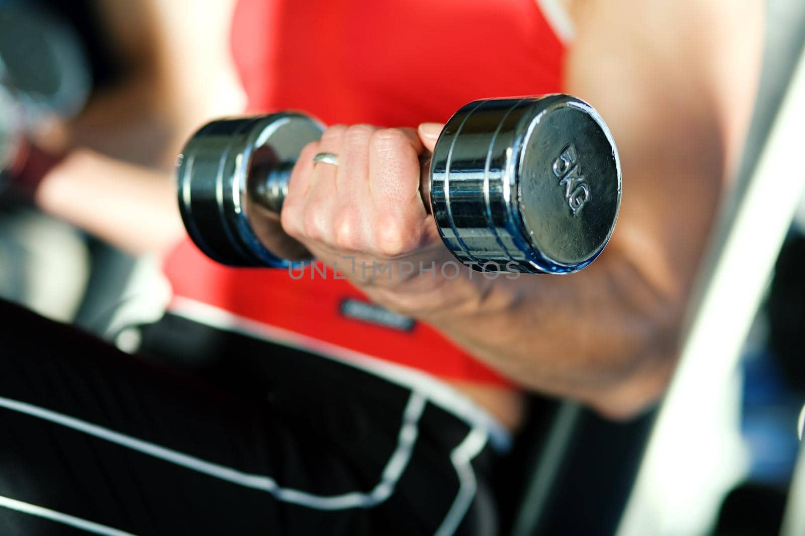 Woman lifting hand weights in a gym, focus on hand of woman and front of dumbbell