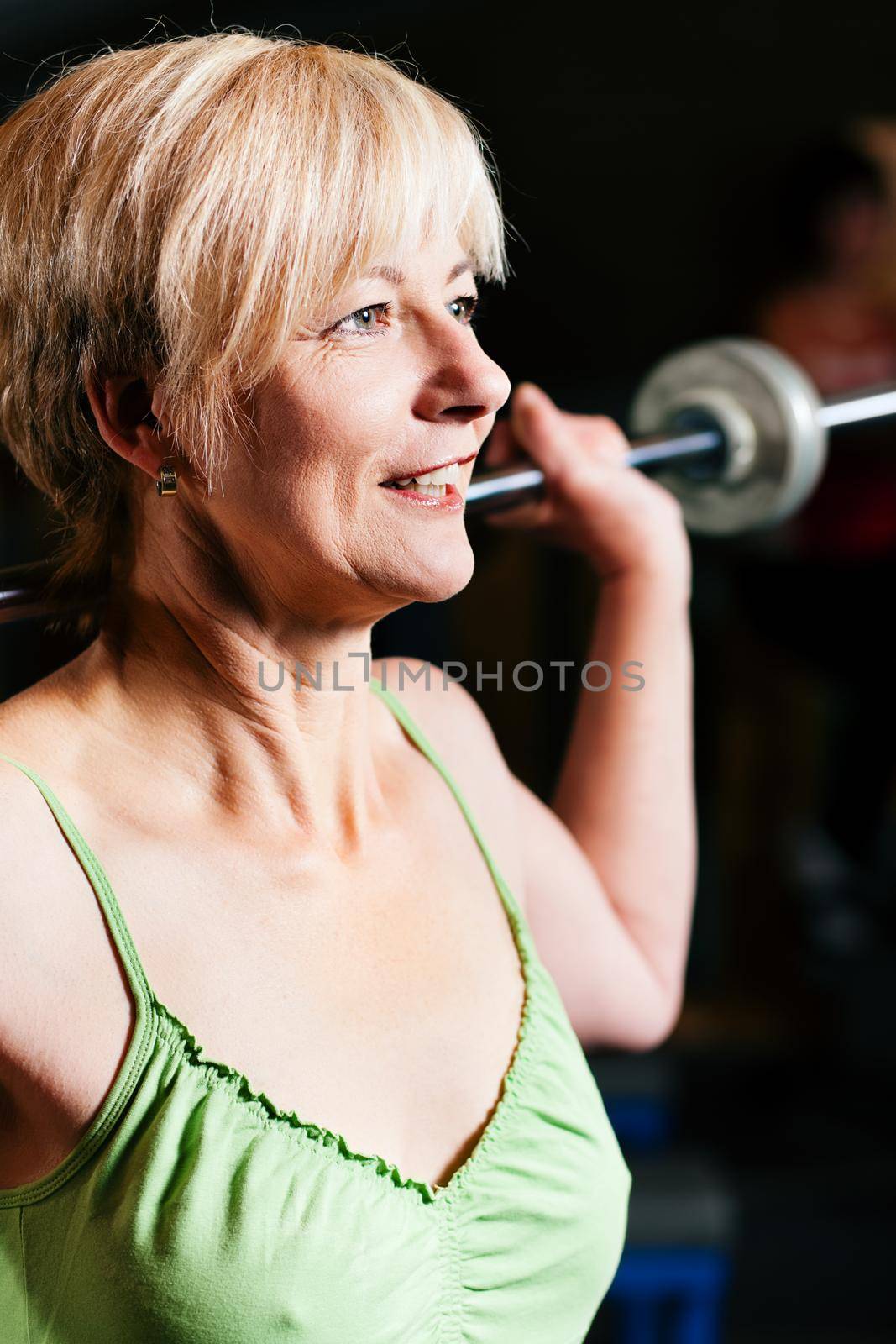 Senior woman in a gym exercising with barbell