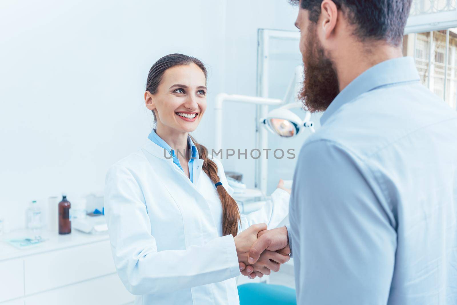 Portrait of a reliable and cheerful dentist shaking the hand of a patient by Kzenon