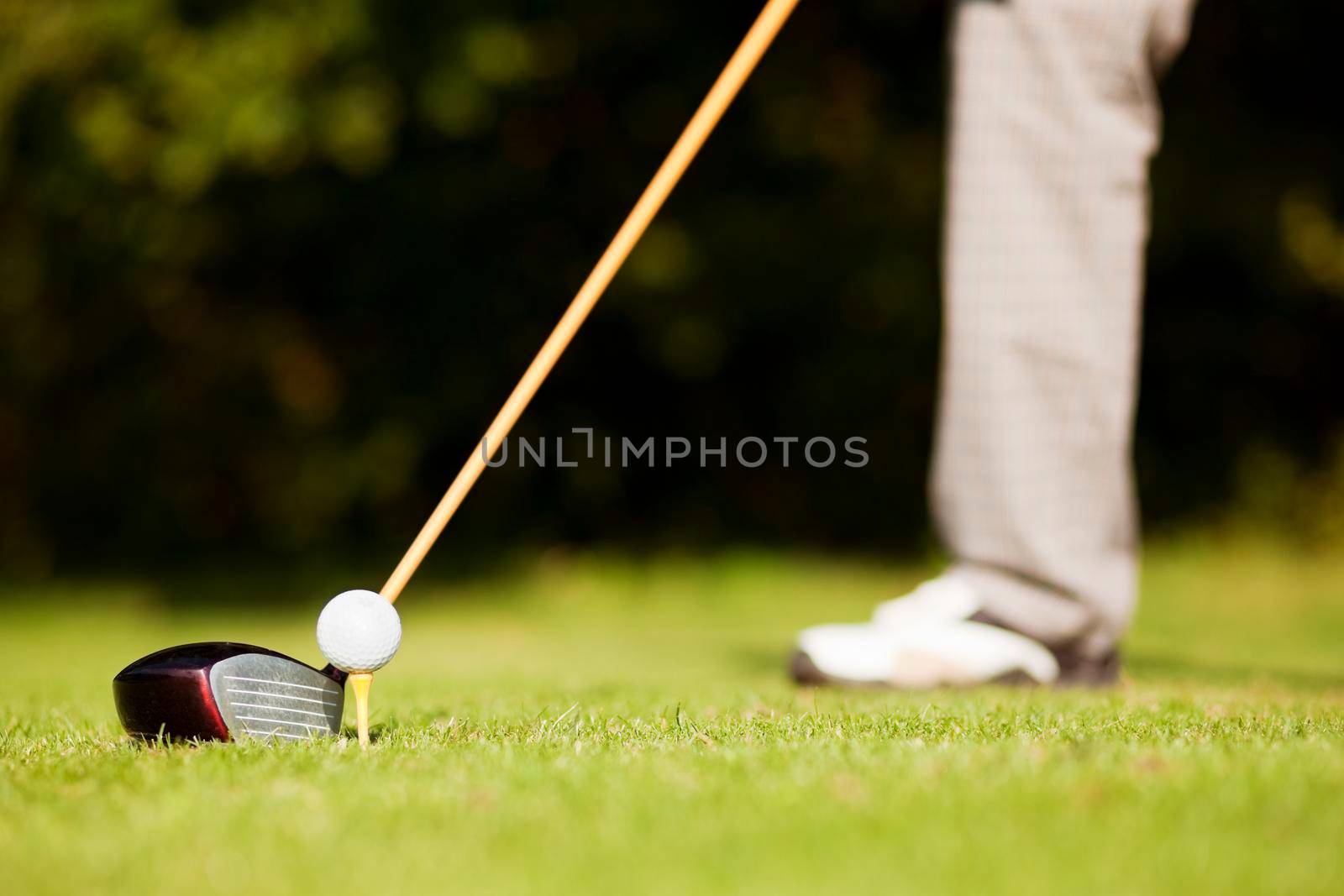 Golf player attempting the tee stroke in the teeing area (only legs of player to be seen, focus on ball)