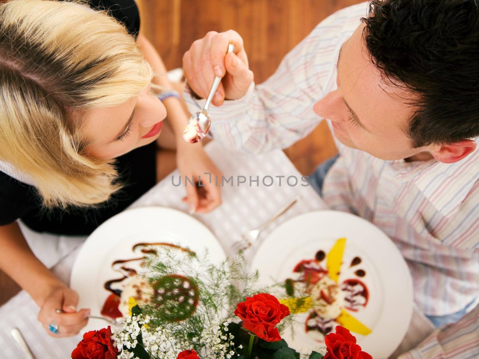 Young couple romantic dinner: he is feeding her with desert (yoghurt mousse); focus on faces
