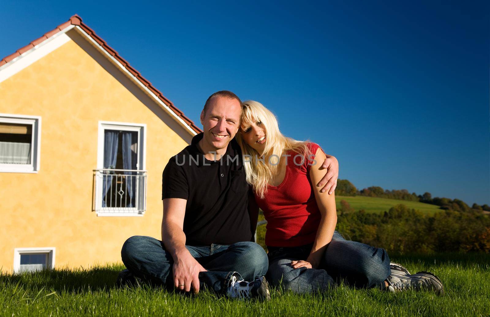Young couple sitting in front of their country house under a perfect blue evening sky