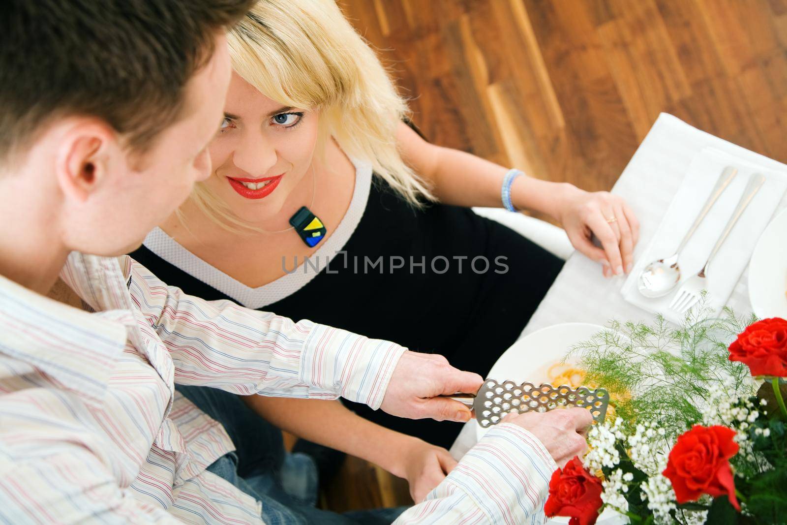 Young couple romantic dinner: he is grating cheese over her pasta; focus on face of the girl