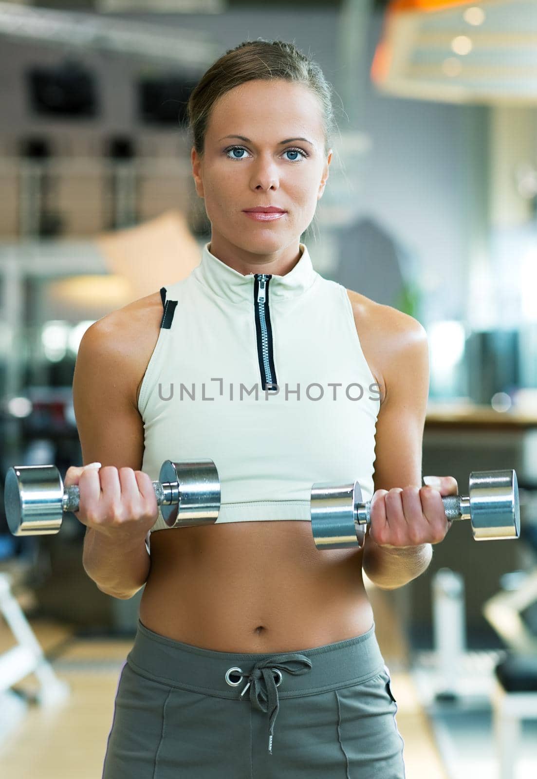 Beautiful young woman exercising with dumbbells in the gym