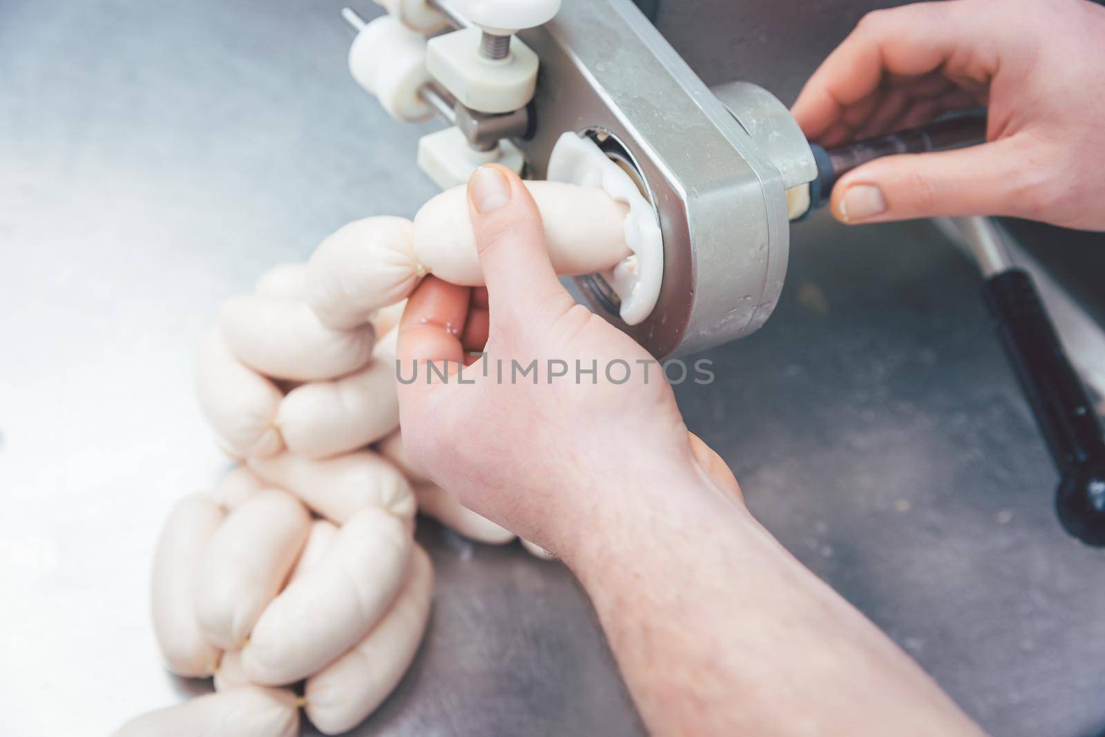 Butcher in butchery filling sausages on a chain