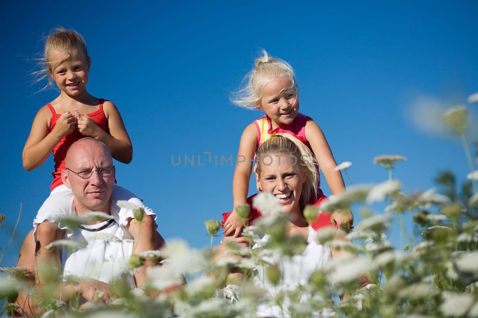 A young family with two cute daughters sitting on the shoulders of the parents, all in a field of yarrow