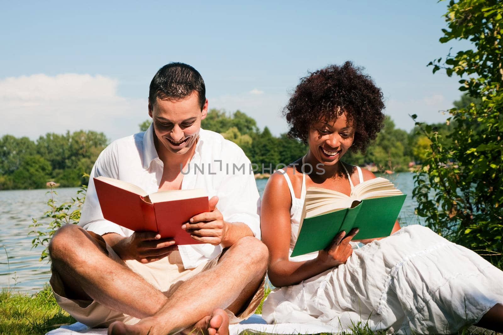 Couple reading books in the sunshine sitting at lake in summerCouple reading books in the sunshine sitting at lake in summer