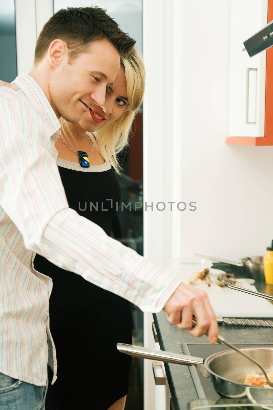 Young couple in their kitchen at home: She is admiring him for his marvellous ability to cook
