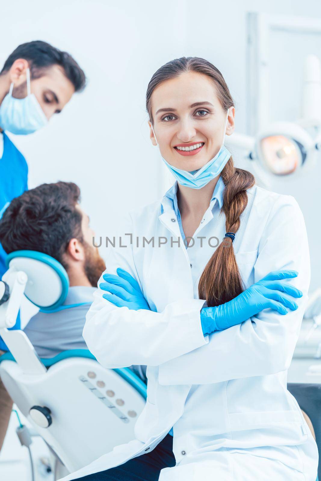 Portrait of a happy and confident female dentist wearing sterile white coat and surgical gloves, while looking at camera in the dental office of a modern clinic with reliable specialists