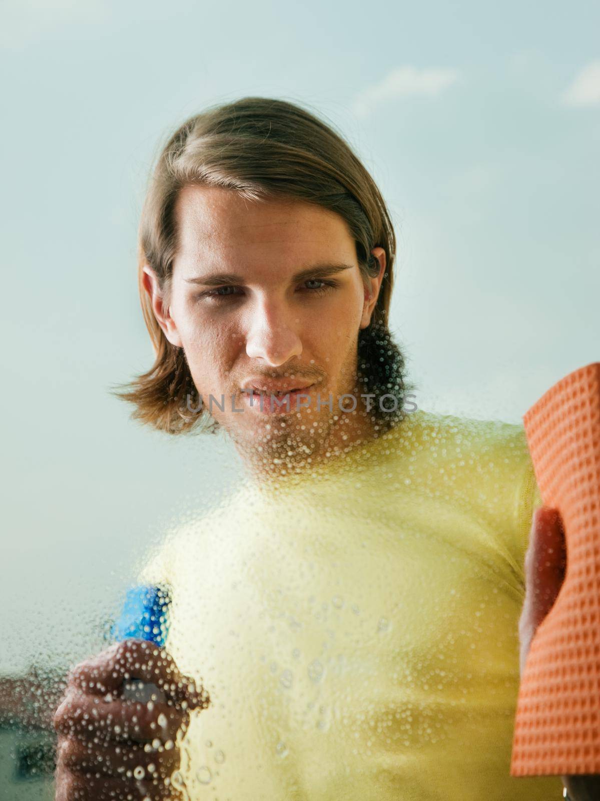 Young man cleaning his windows with spray and sponge