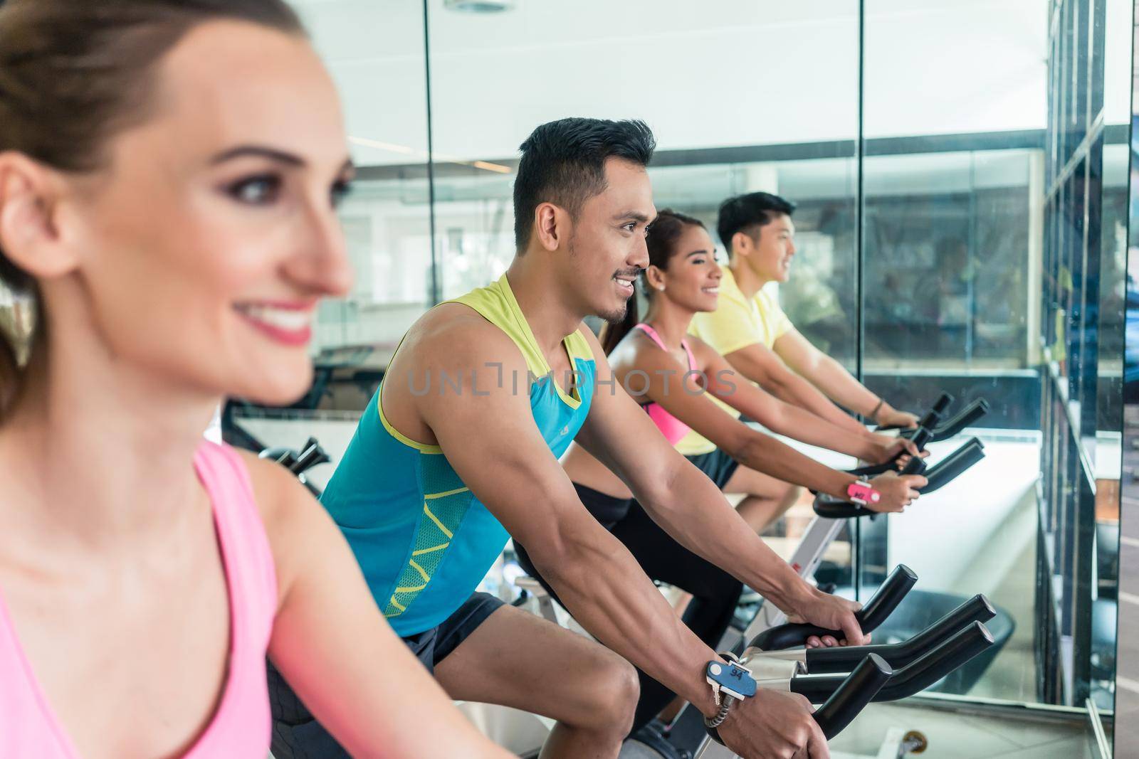 Side view of a beautiful fit young woman smiling while pedaling during cardio workout at indoor cycling group class in a modern fitness club