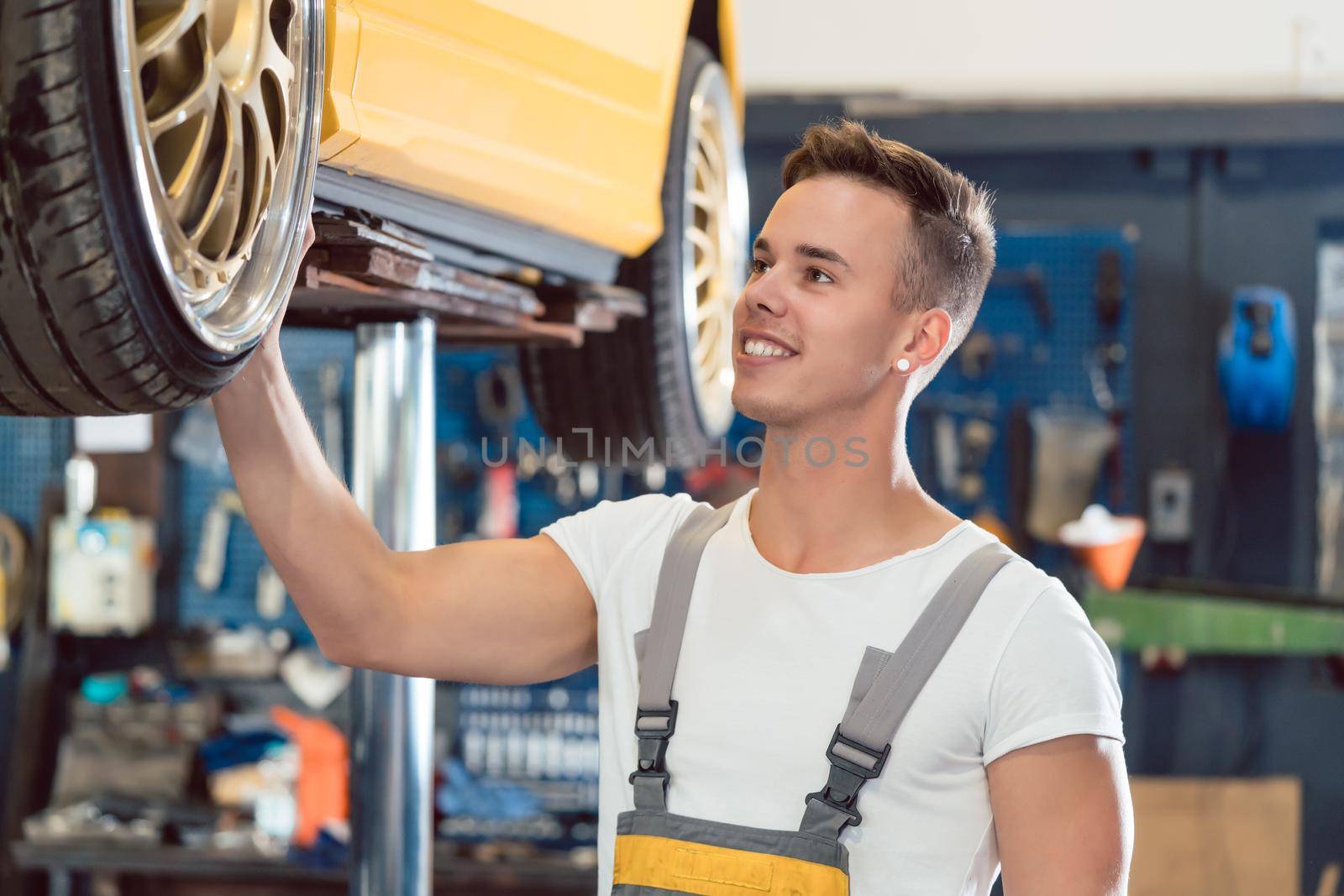 Portrait of a car tuning specialist smiling while checking wheels of tuned car by Kzenon