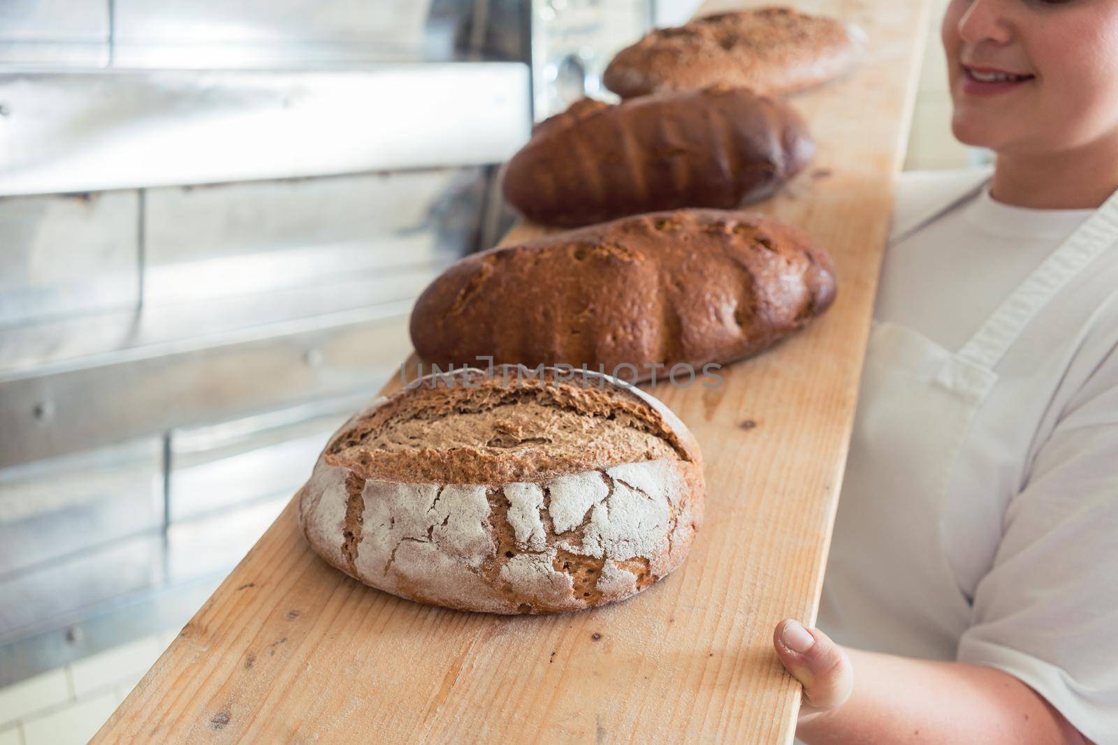 Fresh bread on a board in bakehouse of bakery being held by a female baker