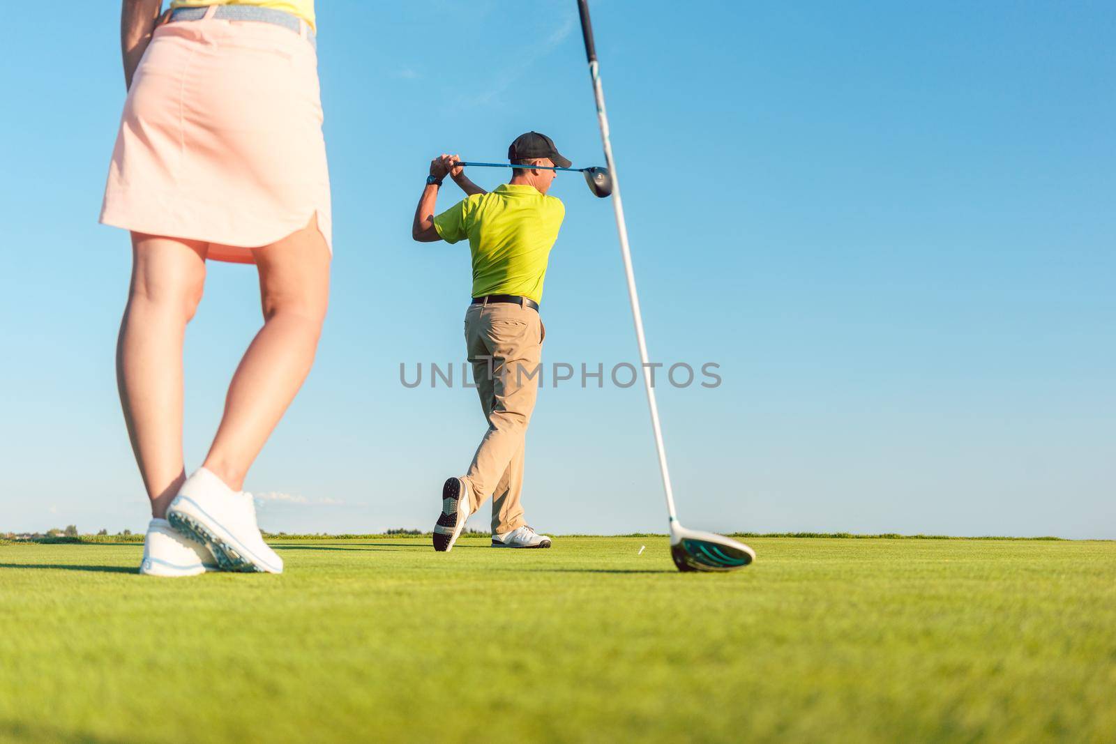 Low-angle full length view of man playing professional golf with his female partner during matchplay, for two players outdoors in a sunny day of summer