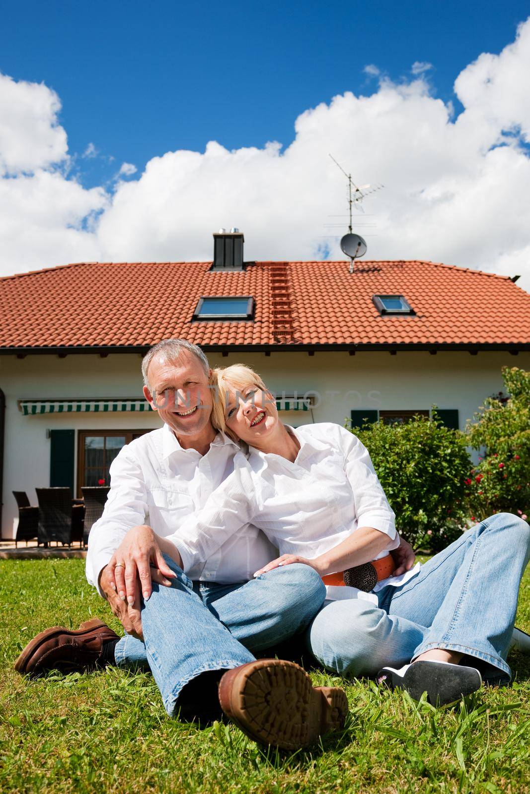 Senior couple sitting in front of their home by Kzenon