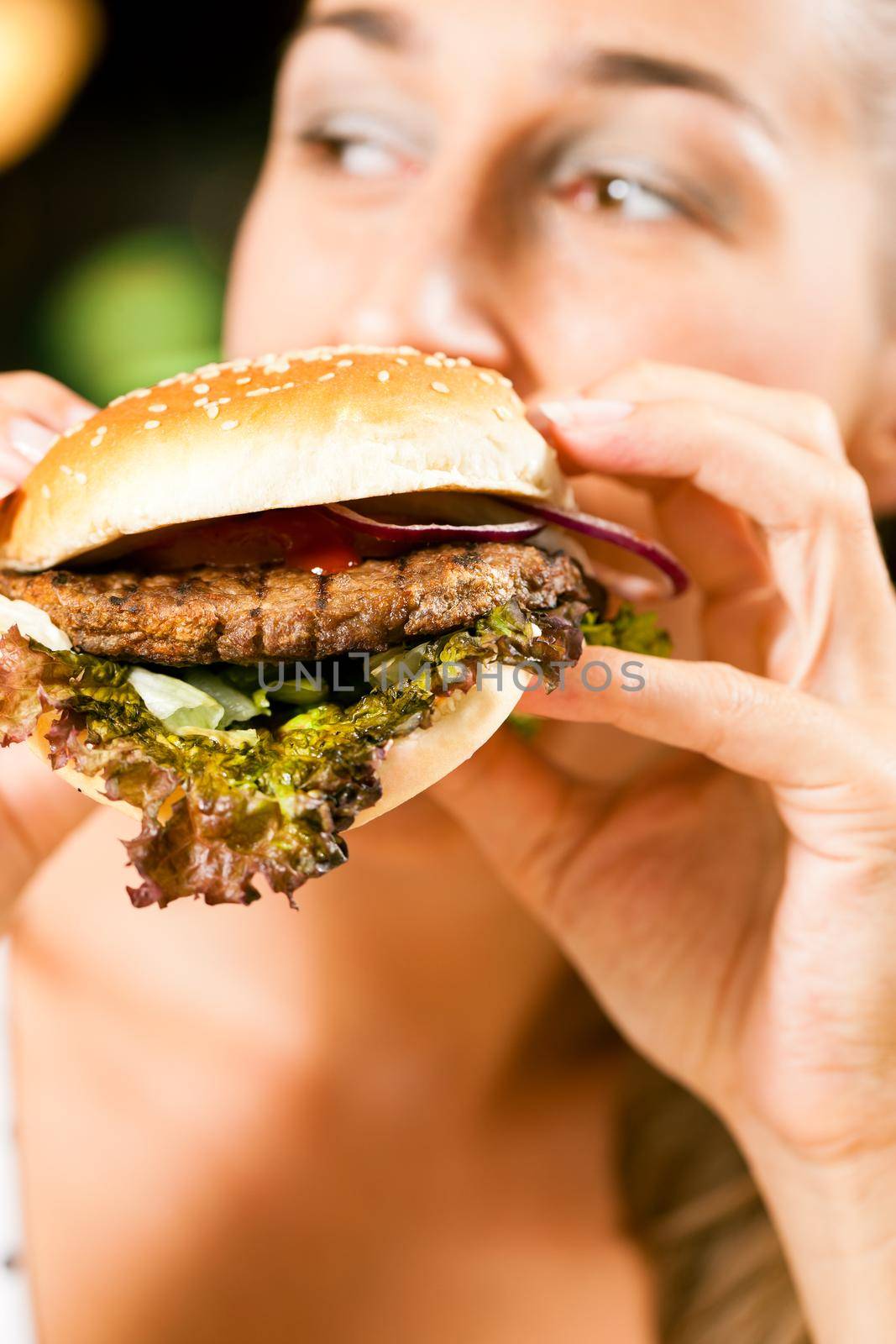 Happy woman in a restaurant eating a fast food hamburger, focus on the burger