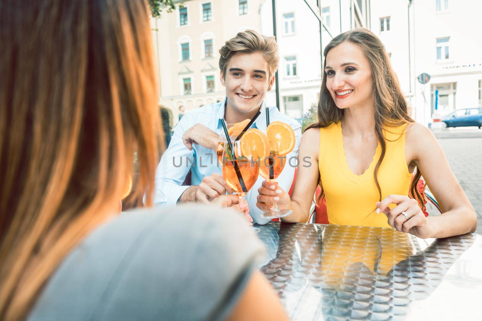 Happy couple toasting with their mutual female friend at a trendy restaurant by Kzenon