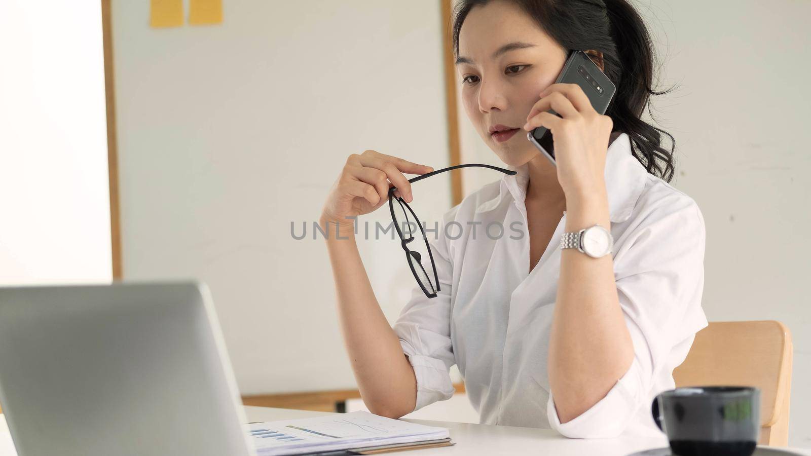 Young female entrepreneur working laptop computer and talking mobile phone by nateemee