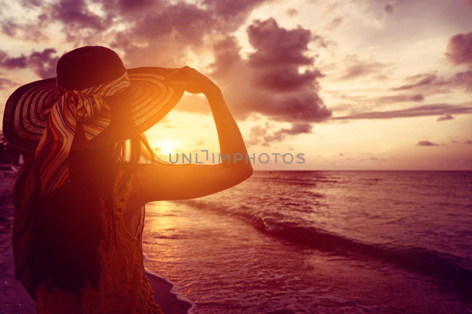 Tourist woman watching sunset at tropical ocean beach